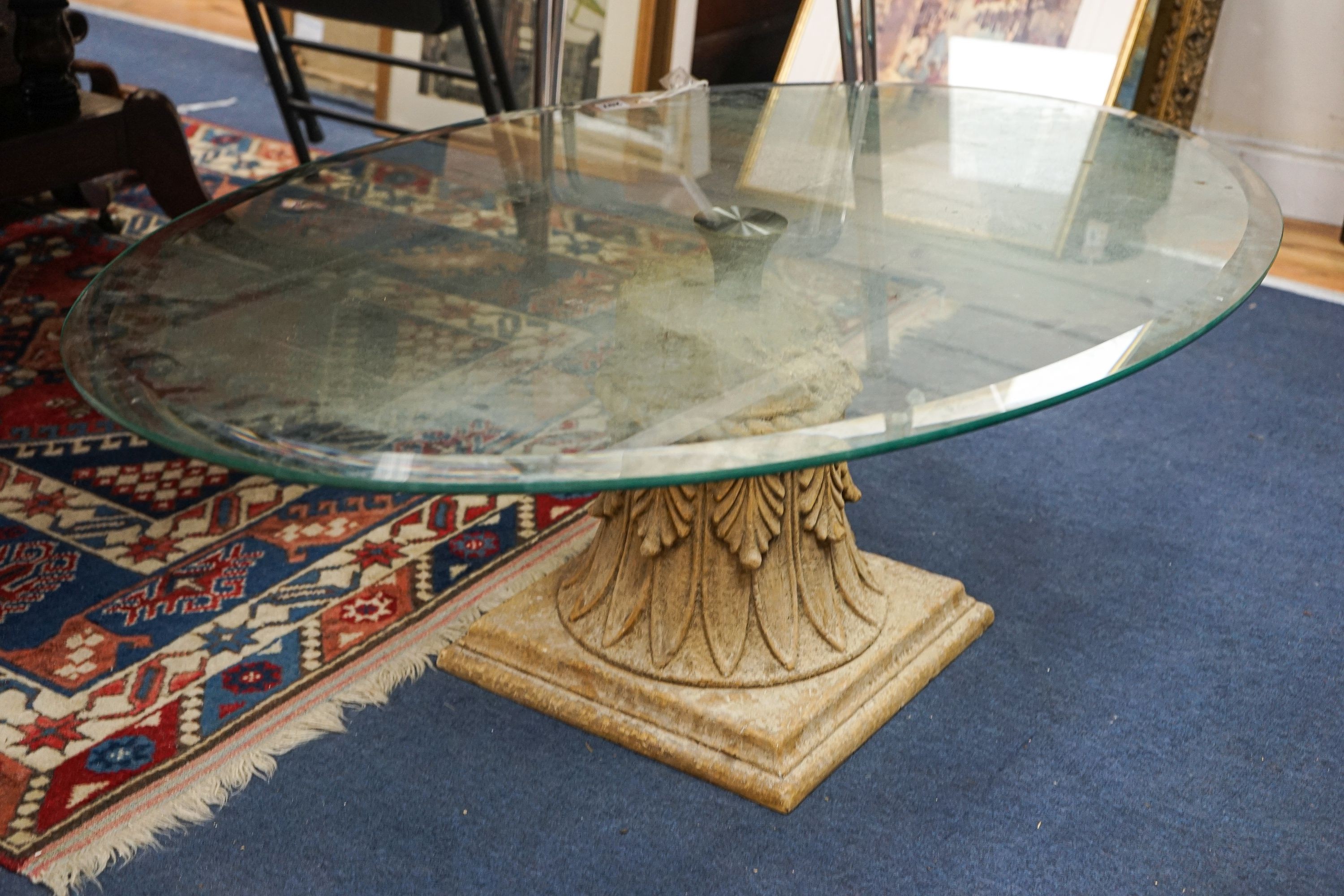 A contemporary oval glass top coffee table on simulated carved stone base, width 118cm, depth 79cm, height 41cm